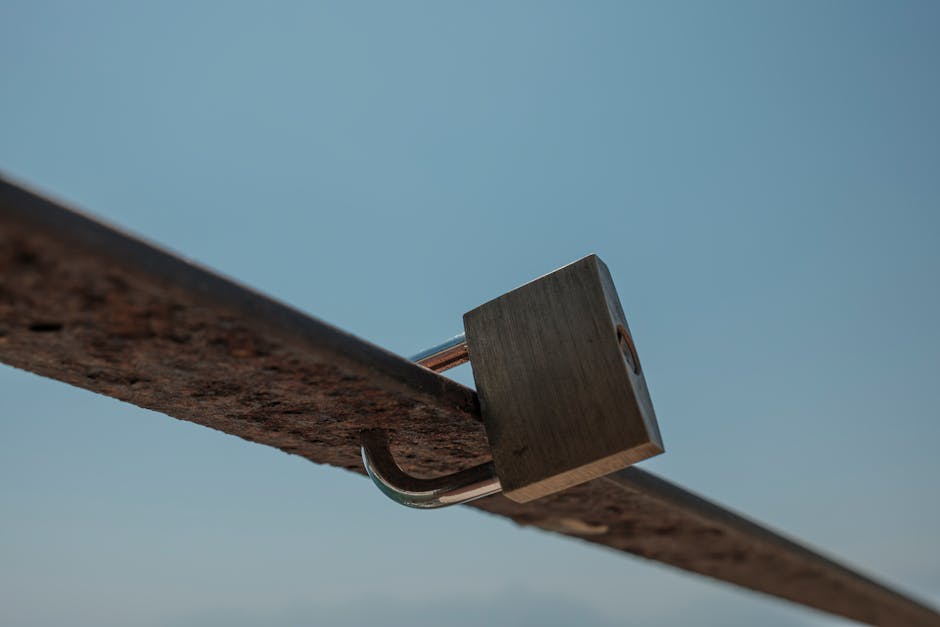 A detailed view of a padlock attached to a rusted metal beam against a clear blue sky.